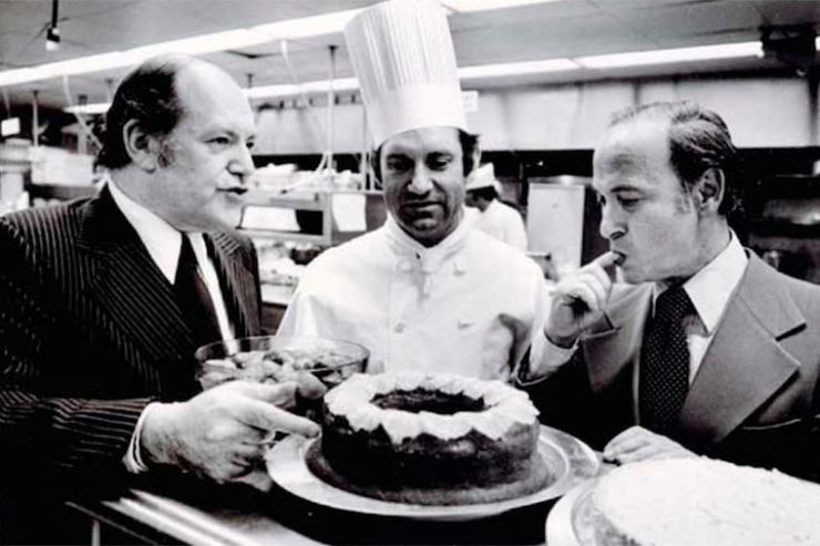 black and white photo of jow baum pointing at a freshly baked pie with chef looking on