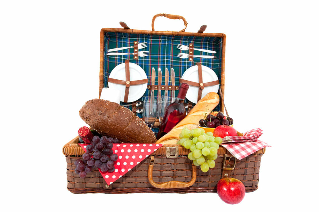 an open wicker picnic basket overflowing with food and wine