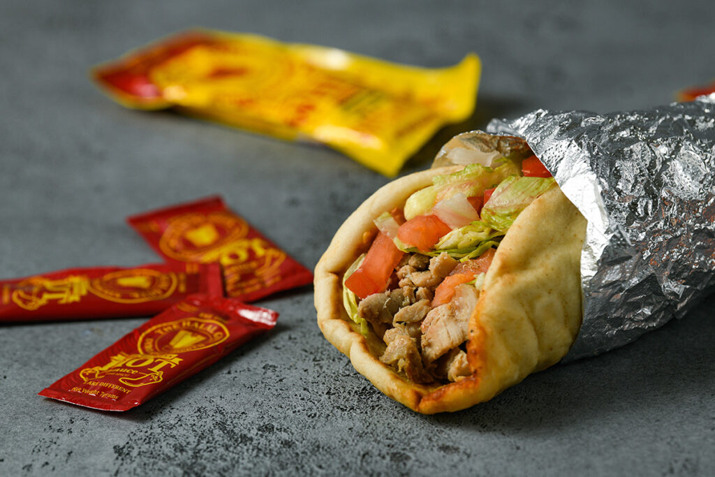 halal guys chicken sandwich in foil with sauce packets around