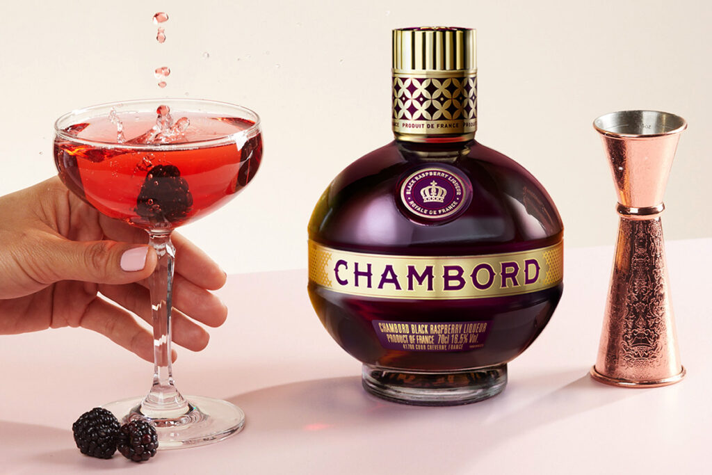 red chambord royale cocktails with blackberries in it next to a bottle of chambord and a rose gold jigger 