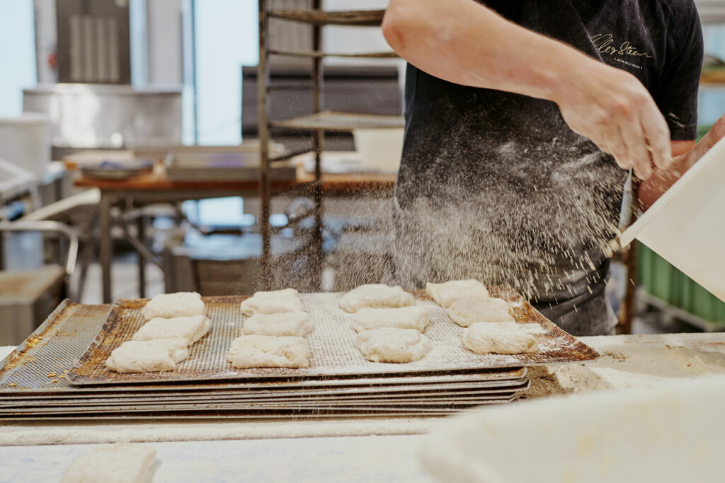 a baker sprinkling flour over unbaked pastries