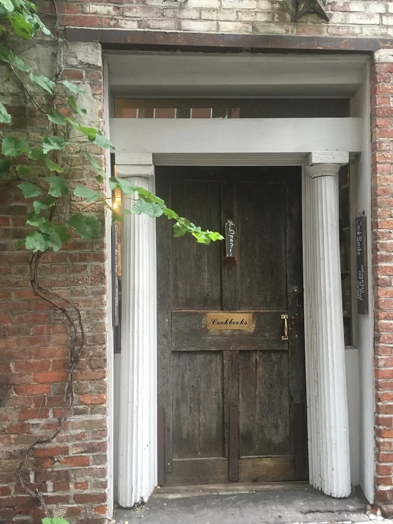 a wooden door in a brick facade, flanked by white columns. the brass plate on the door reads "cookbooks"