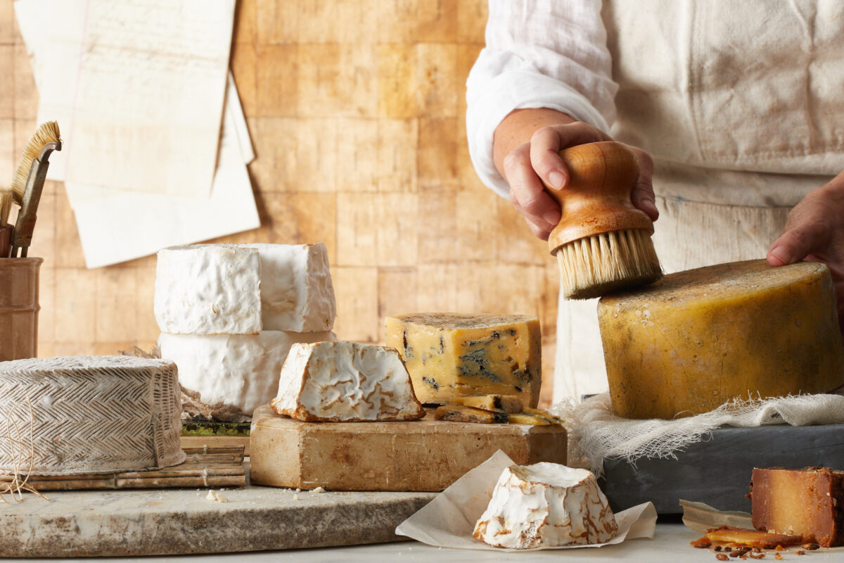 person brushing off a wheel of homemade cheese