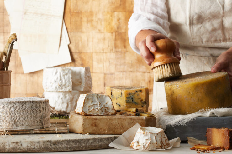person brushing off a wheel of homemade cheese