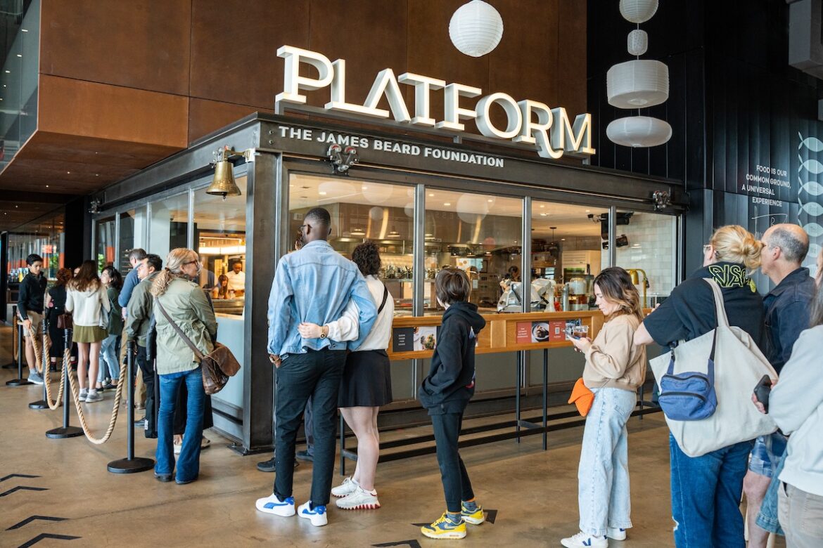 people lining up for food under a platform by james beard foundation sign