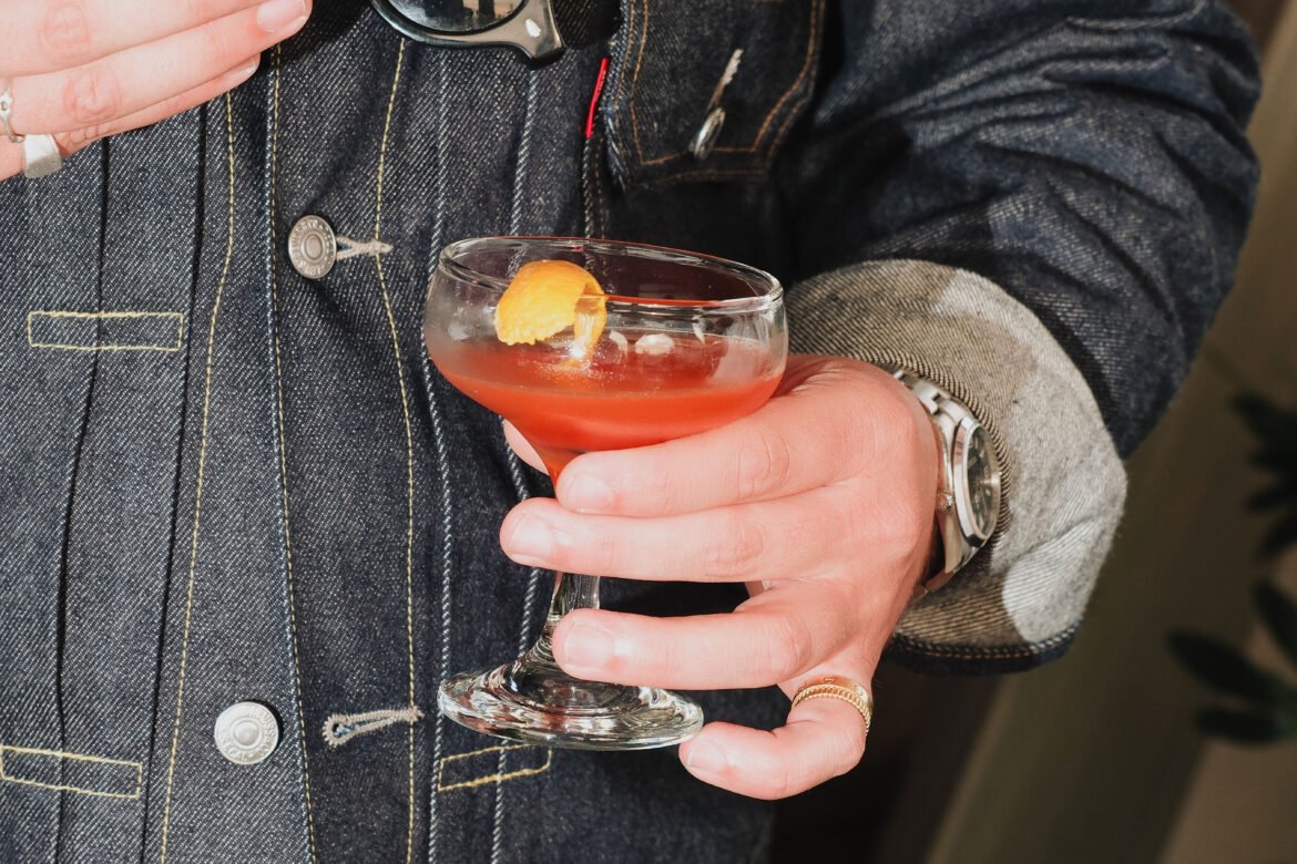 a person in a denim jacket holding a maker's mark cocktail